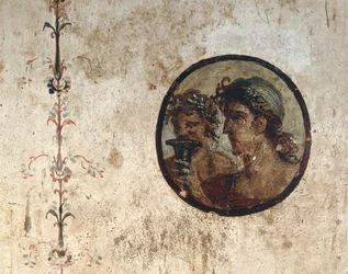 Innenraum eines Zimmers mit Wandfresken aus der römischen Zeit, Stil III, im Haus von Corieo Tiburtino in Pompeji: Teil einer Rebe und ein Tondo mit zwei männlichen Köpfen